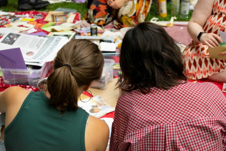 Two person photographed from the back. In front of them lots of magazines to use to cutouts.