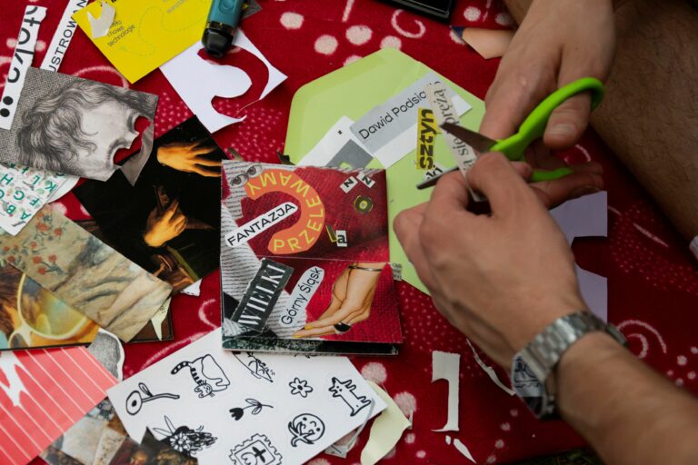 A man's hands cutting out words with scissors from a newspaper over lots of other cut-out images and texts.