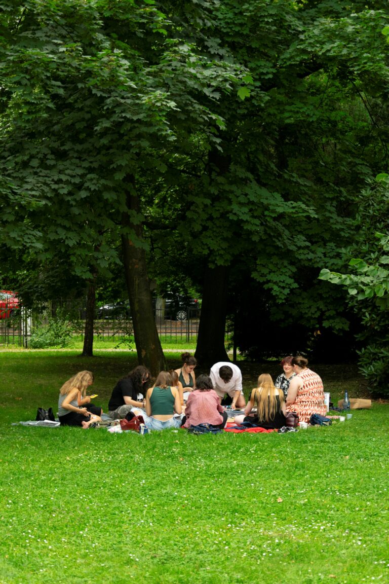 A group of people, participants of the zine workshops, sitting on a grass under the tree.